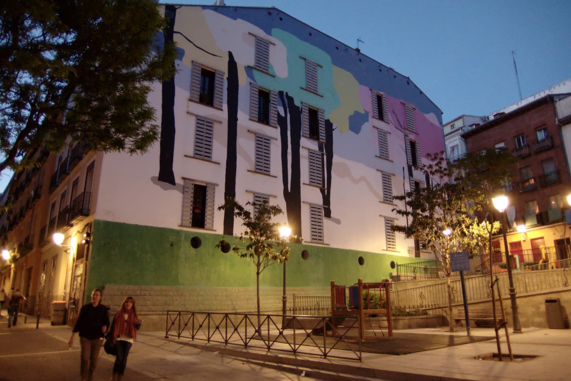 A sloping street in Lavapiés, Madrid, with balconies, shutters and shopfronts on both sides.