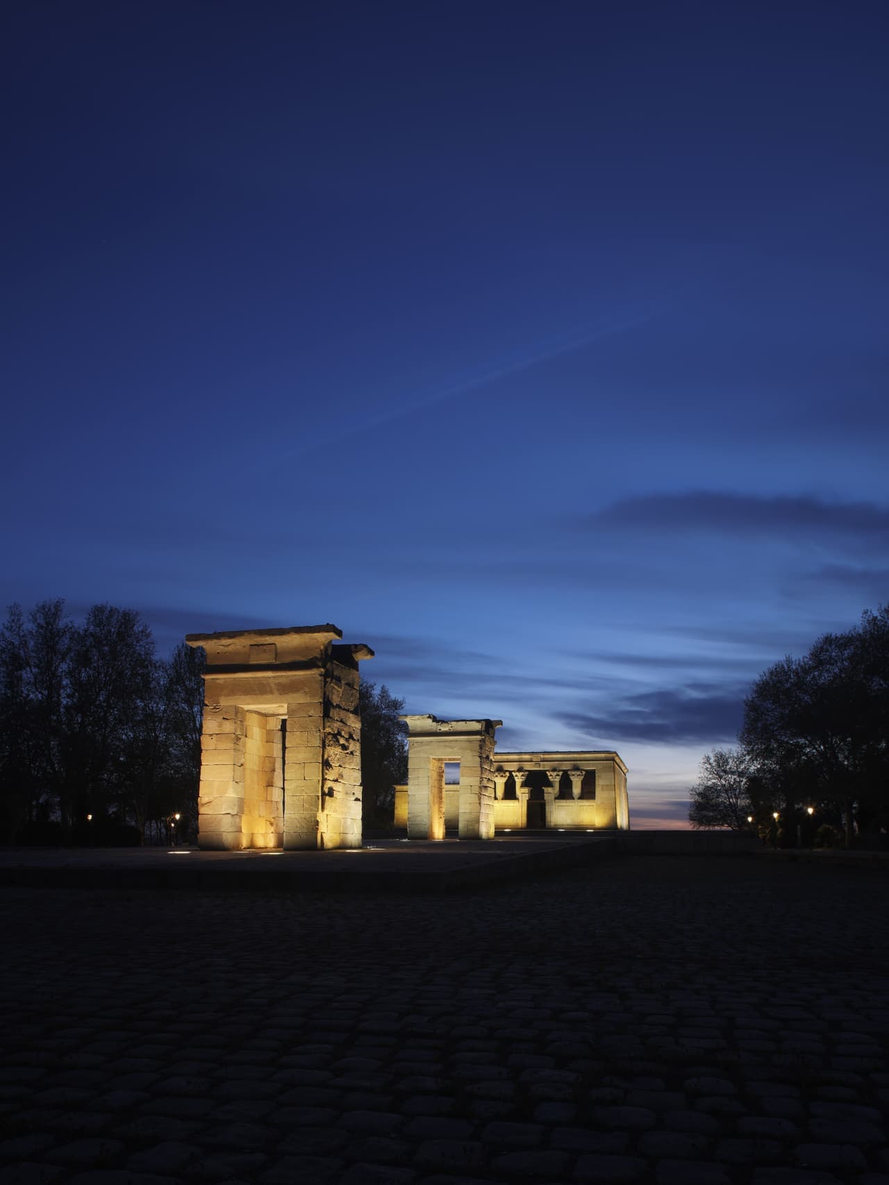 The ancient Egyptian Templo de Debod reflected in its pool in Madrid, silhouetted against an orange evening sky.